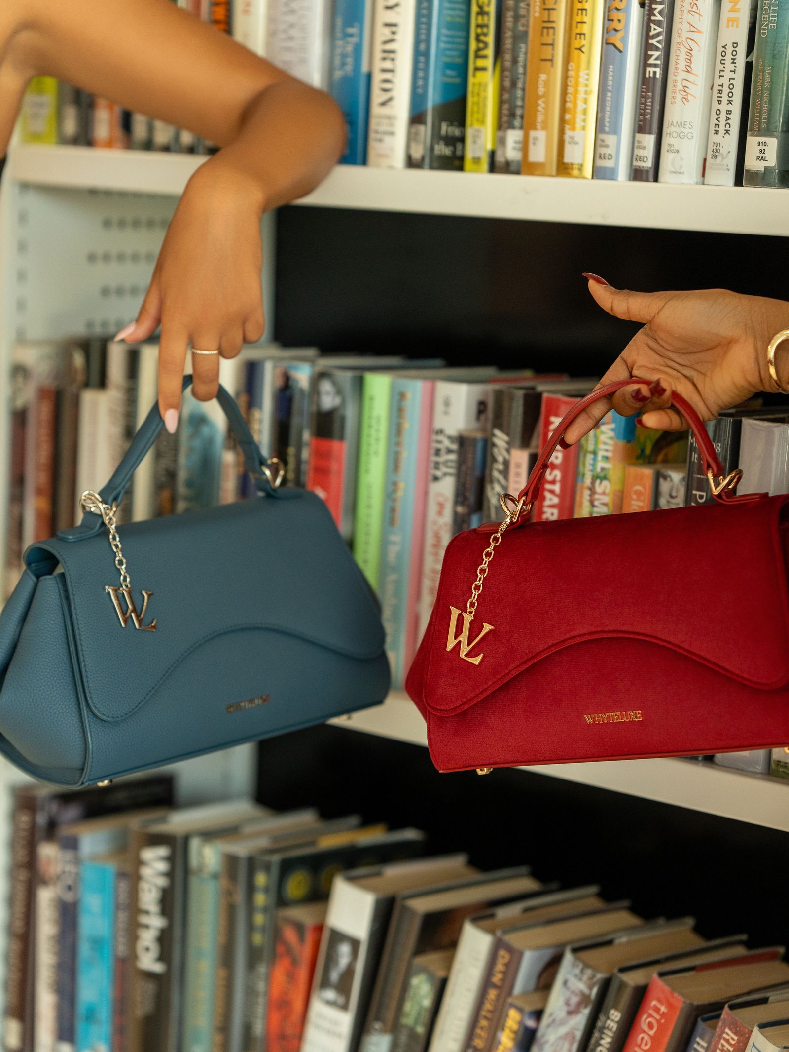 The Becoming bags in Deep Teal and Rouge held against a bookshelf